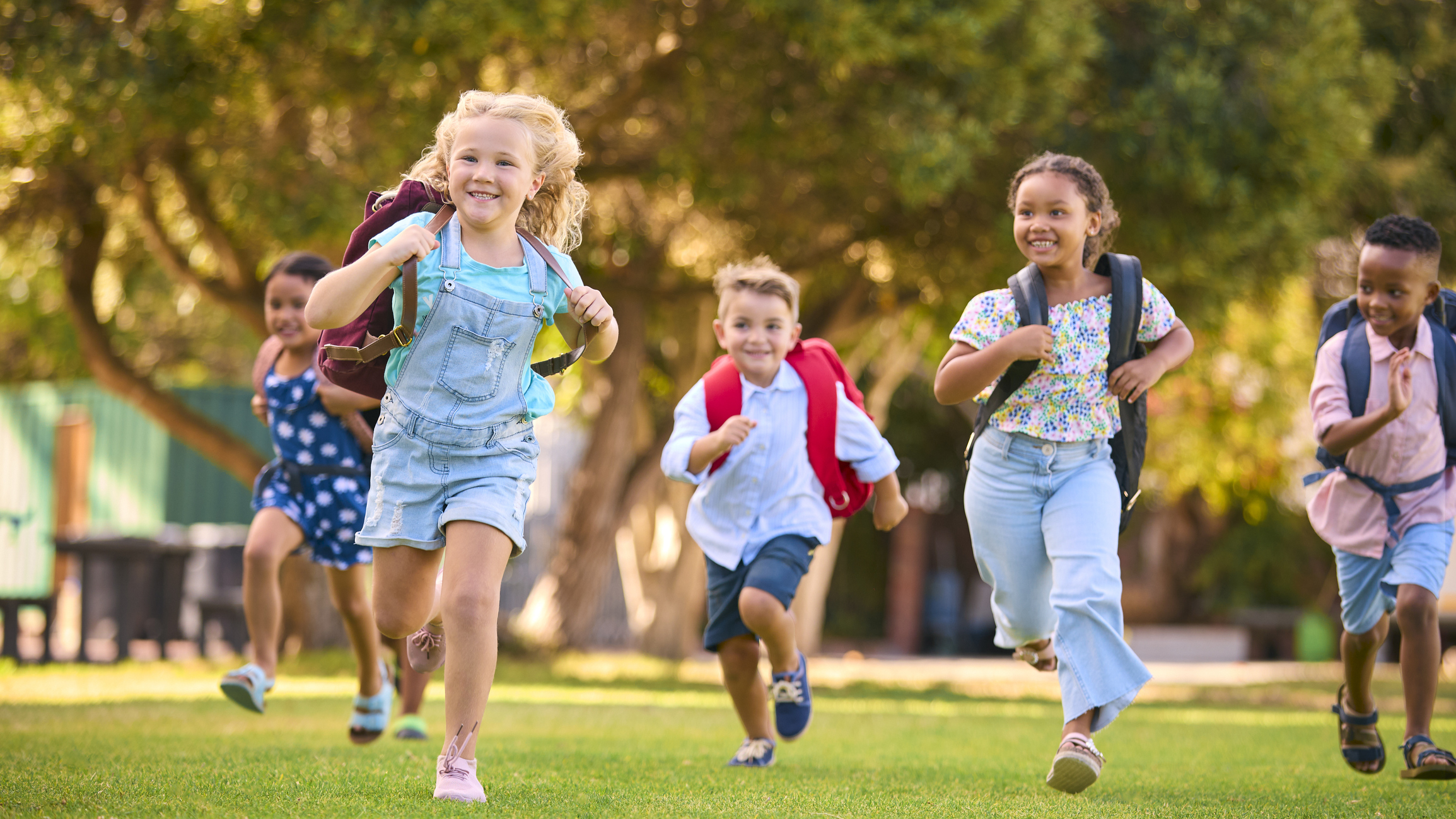 Elementary School Students With Backpacks Running Outdoors