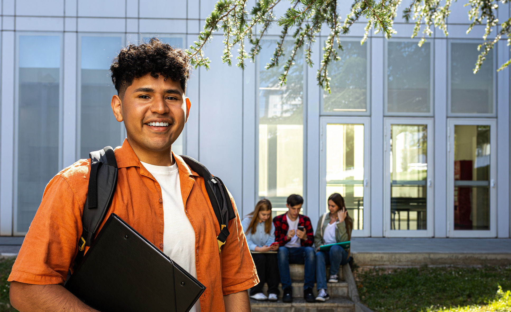Happy smiling hispanic male teen student at school holding books looking at camera. Copy space.